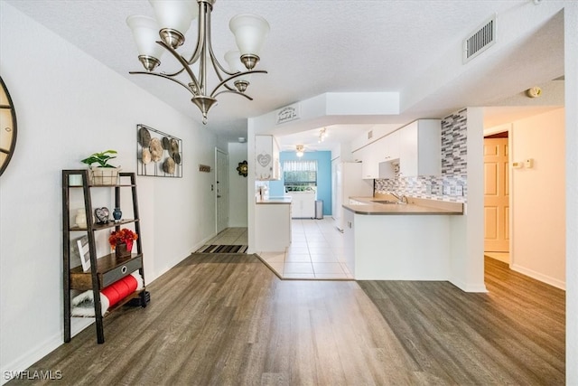 kitchen featuring kitchen peninsula, backsplash, pendant lighting, light wood-type flooring, and white cabinets