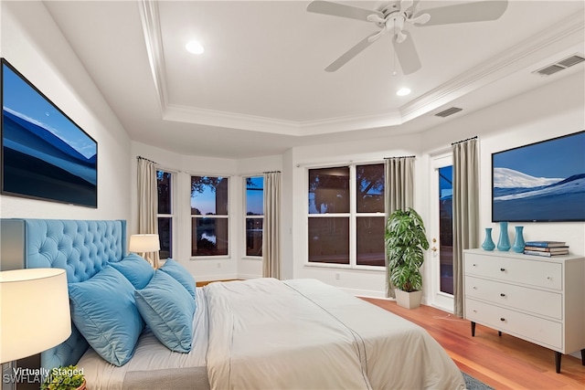 bedroom with ceiling fan, a tray ceiling, light wood-type flooring, and ornamental molding