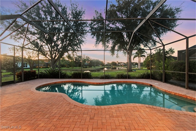 pool at dusk featuring glass enclosure and a patio