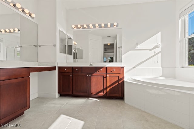 bathroom with a relaxing tiled tub, vanity, and tile patterned flooring