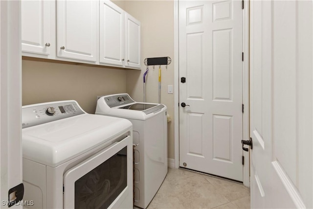 clothes washing area featuring cabinets, light tile patterned flooring, and washer and clothes dryer