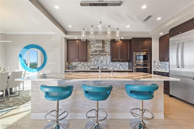 kitchen with built in appliances, wall chimney exhaust hood, hanging light fixtures, and a large island