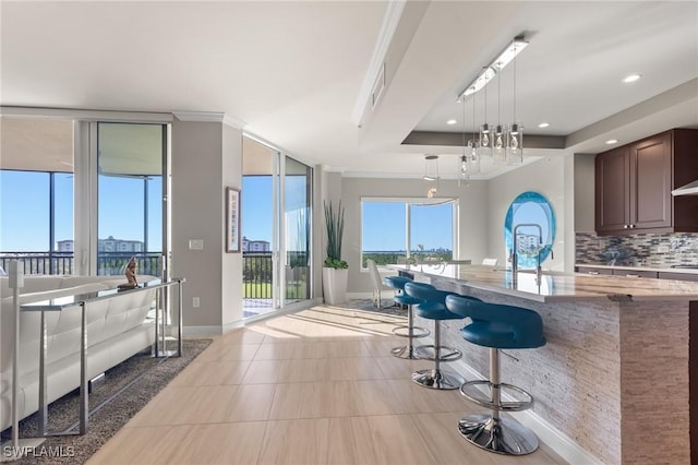 kitchen with decorative backsplash, pendant lighting, a raised ceiling, a breakfast bar, and a wall of windows