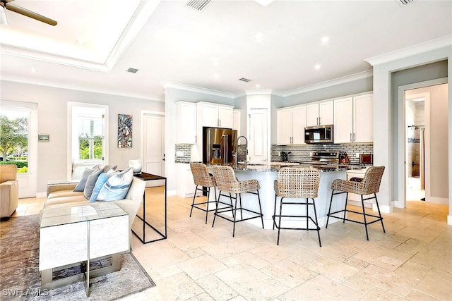 kitchen with white cabinetry, tasteful backsplash, stainless steel appliances, a kitchen bar, and ornamental molding