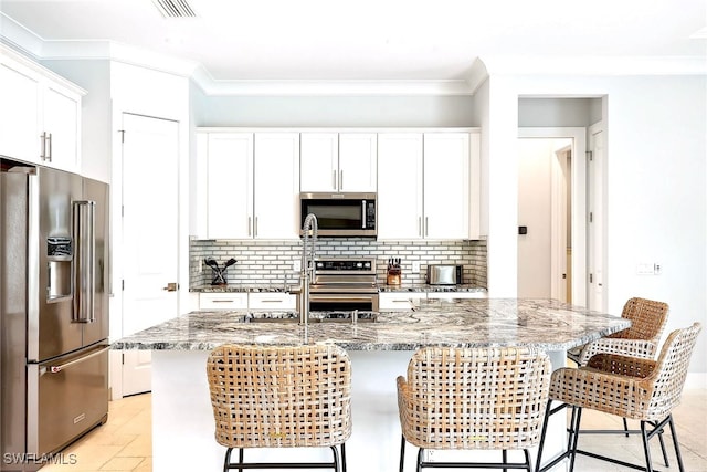 kitchen with light stone counters, white cabinets, an island with sink, stainless steel appliances, and a kitchen bar