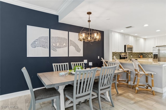 dining room featuring ornamental molding, sink, a chandelier, and light hardwood / wood-style flooring