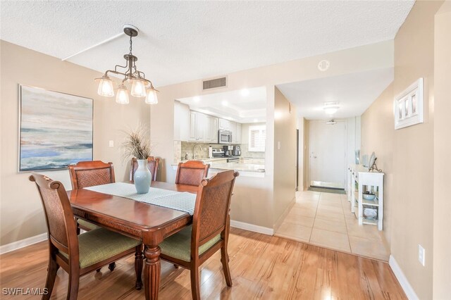 dining space with light hardwood / wood-style flooring, a chandelier, a textured ceiling, and sink