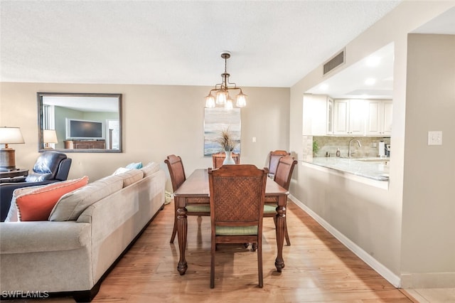 dining area featuring a notable chandelier, sink, light hardwood / wood-style floors, and a textured ceiling