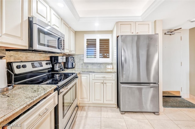 kitchen with light stone counters, light tile patterned flooring, backsplash, stainless steel appliances, and a tray ceiling