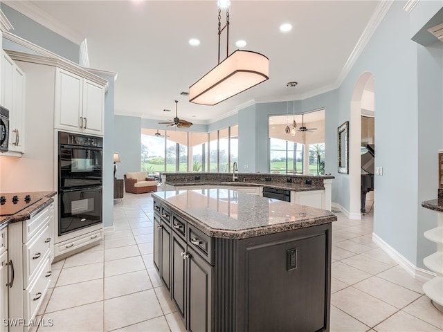 kitchen with dark stone counters, a kitchen island, black appliances, light tile patterned floors, and ornamental molding