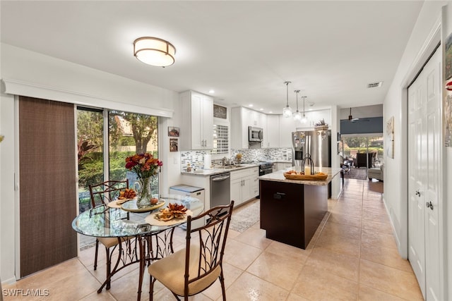 kitchen featuring appliances with stainless steel finishes, hanging light fixtures, white cabinets, backsplash, and a center island