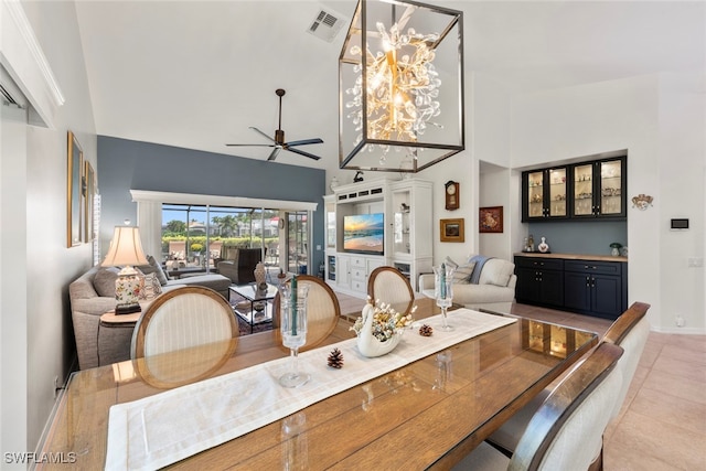 dining room with light tile patterned flooring, ceiling fan with notable chandelier, and a high ceiling