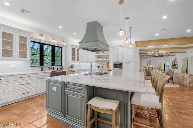 kitchen featuring a large island with sink, light stone countertops, white cabinets, and custom exhaust hood