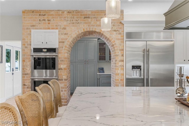 kitchen with light stone countertops, brick wall, stainless steel appliances, decorative light fixtures, and gray cabinets