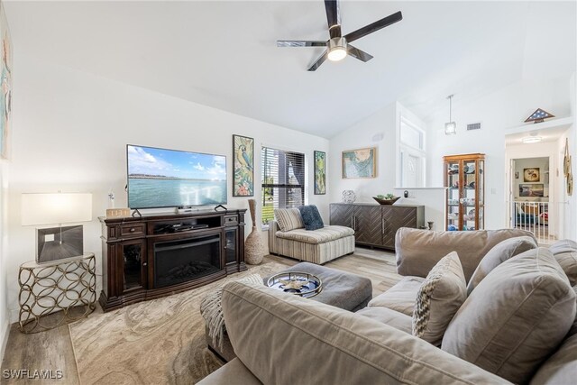 living room featuring ceiling fan, light wood-type flooring, a fireplace, and high vaulted ceiling