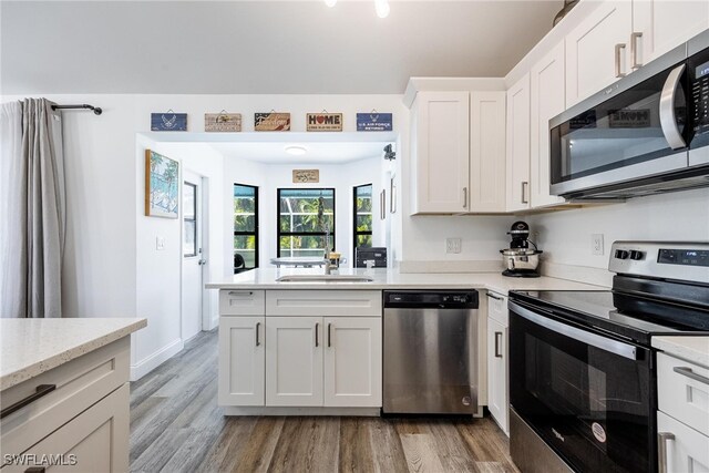 kitchen with sink, light wood-type flooring, appliances with stainless steel finishes, light stone counters, and white cabinetry