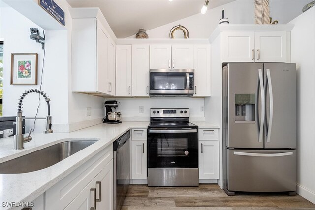 kitchen with sink, white cabinets, vaulted ceiling, and appliances with stainless steel finishes