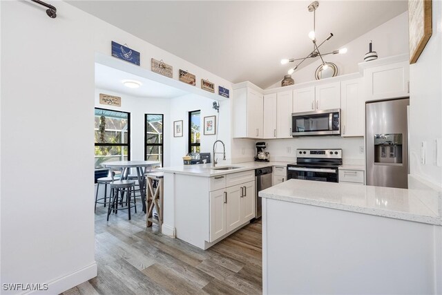 kitchen featuring white cabinets, hanging light fixtures, vaulted ceiling, kitchen peninsula, and stainless steel appliances