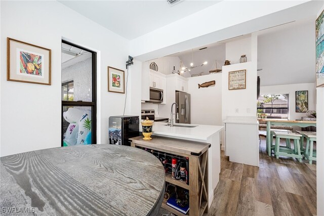 kitchen featuring white cabinetry, hanging light fixtures, stainless steel appliances, an island with sink, and hardwood / wood-style flooring