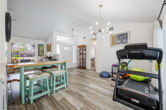 exercise area featuring high vaulted ceiling, light hardwood / wood-style floors, and an inviting chandelier