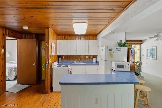 kitchen with white cabinetry, white appliances, light wood-type flooring, wooden walls, and sink