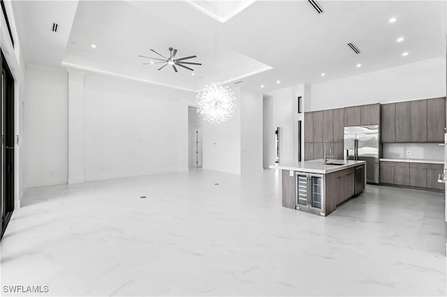 kitchen featuring stainless steel built in refrigerator, sink, a kitchen island with sink, a tray ceiling, and an inviting chandelier