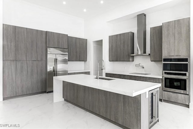 kitchen with an island with sink, sink, wine cooler, stainless steel appliances, and wall chimney range hood