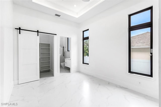 unfurnished bedroom featuring a tray ceiling, a barn door, and ensuite bathroom