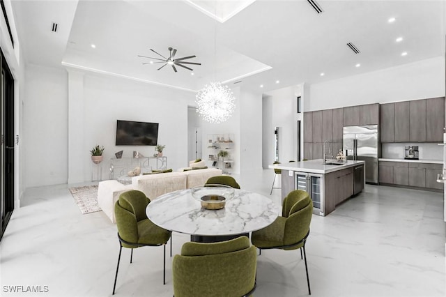 dining room with sink, a chandelier, a tray ceiling, beverage cooler, and a high ceiling