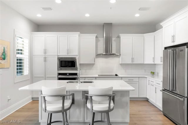 kitchen featuring a center island with sink, appliances with stainless steel finishes, wall chimney exhaust hood, and white cabinetry