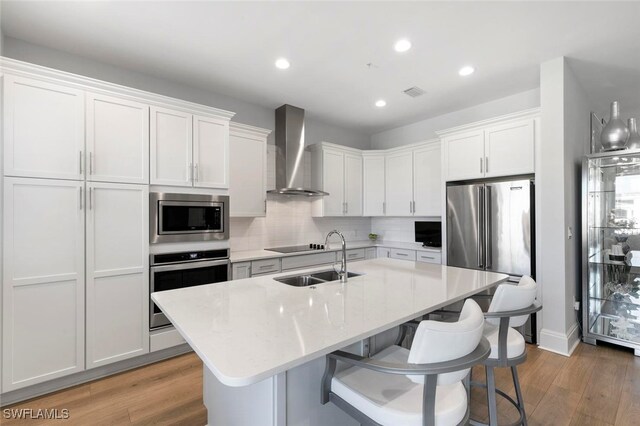 kitchen with wall chimney exhaust hood, light hardwood / wood-style floors, sink, stainless steel appliances, and white cabinets