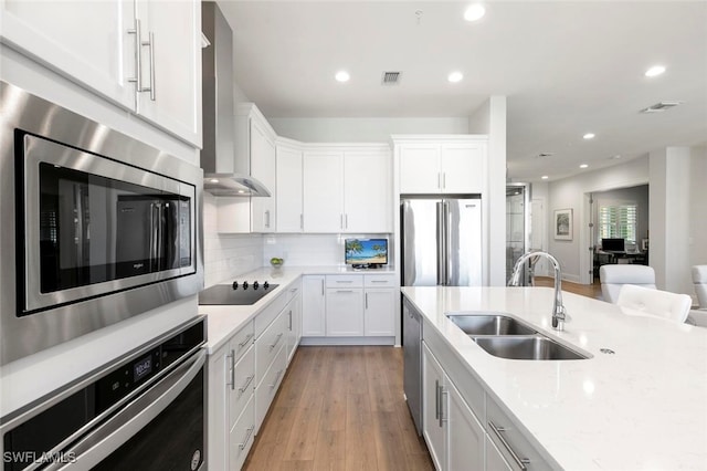 kitchen featuring wall chimney range hood, white cabinets, appliances with stainless steel finishes, and sink