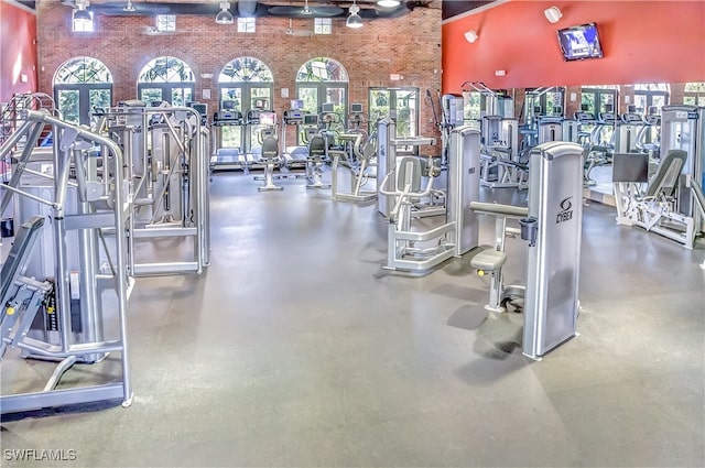 workout area with a wealth of natural light, a towering ceiling, and brick wall