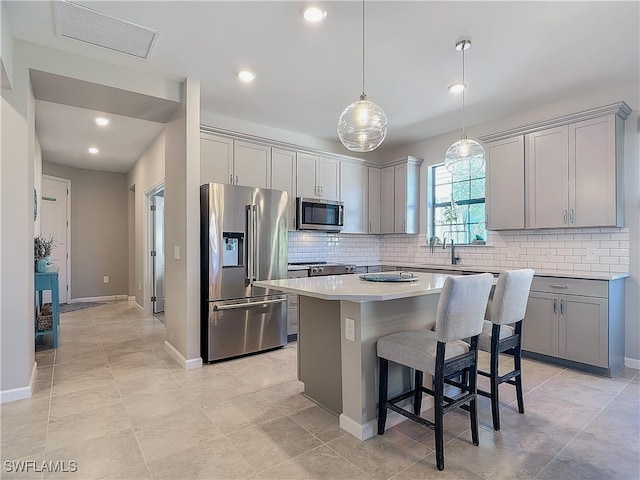 kitchen featuring gray cabinetry, hanging light fixtures, stainless steel appliances, a breakfast bar area, and a kitchen island