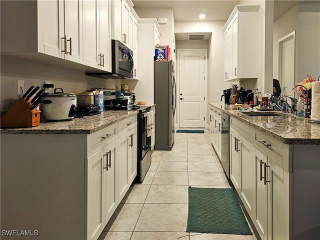 kitchen featuring light tile patterned floors, appliances with stainless steel finishes, white cabinets, and dark stone countertops