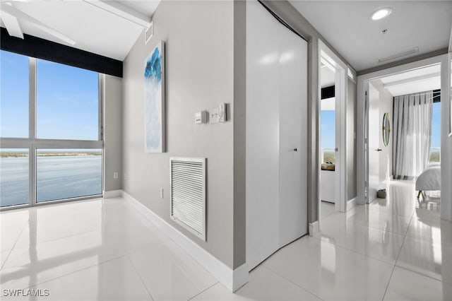 hallway with light tile patterned flooring, a water view, and expansive windows