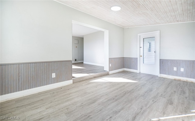 empty room with light wood-type flooring, crown molding, wood walls, and wooden ceiling