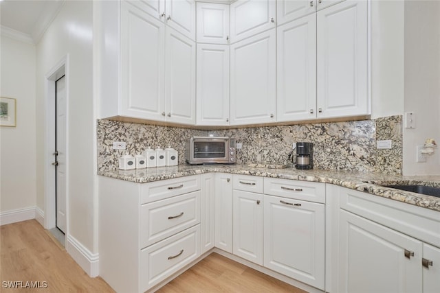 kitchen with light wood-type flooring, crown molding, white cabinetry, and decorative backsplash