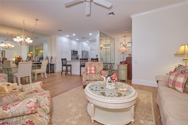 living room featuring ceiling fan with notable chandelier, light wood-type flooring, and ornamental molding