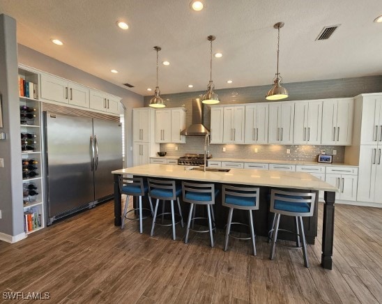 kitchen with wall chimney exhaust hood, dark hardwood / wood-style floors, white cabinets, and built in fridge