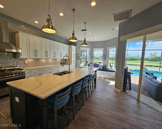 kitchen with a kitchen island with sink, dark hardwood / wood-style floors, sink, wall chimney range hood, and white cabinetry