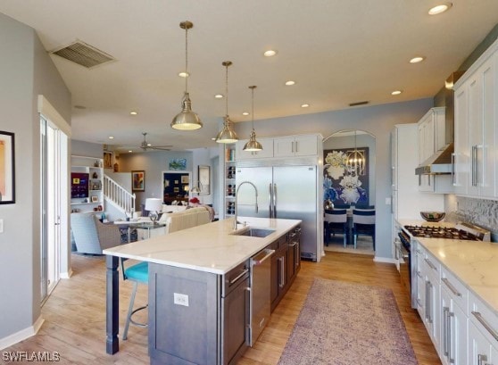 kitchen with white cabinets, an island with sink, hanging light fixtures, appliances with stainless steel finishes, and a breakfast bar area