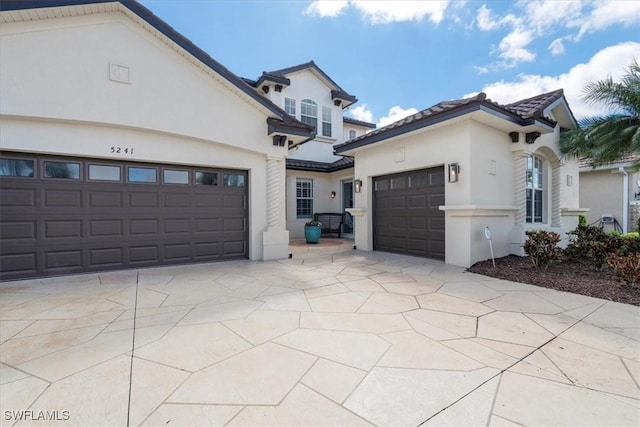 view of front of property with a tile roof, driveway, an attached garage, and stucco siding