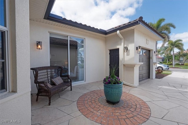 view of exterior entry with driveway, an attached garage, and stucco siding