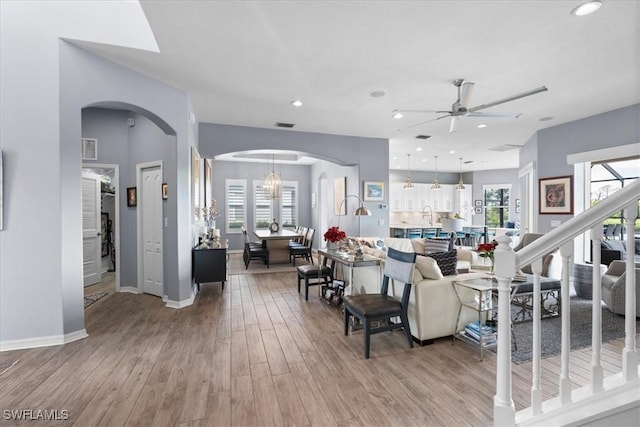 living area with arched walkways, ceiling fan, recessed lighting, baseboards, and light wood-type flooring