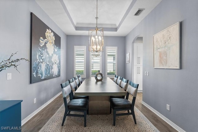 dining area with dark wood-style floors, a notable chandelier, a raised ceiling, visible vents, and baseboards