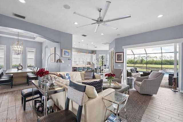 living area with arched walkways, recessed lighting, ceiling fan with notable chandelier, visible vents, and light wood finished floors