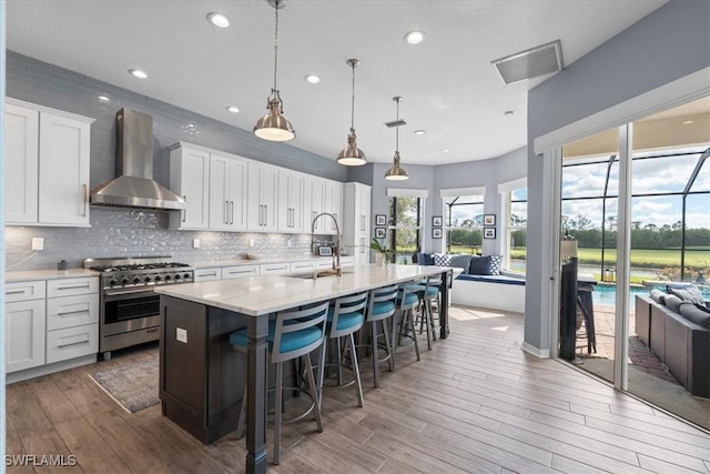 kitchen with stainless steel stove, a sink, visible vents, wall chimney range hood, and backsplash