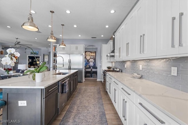 kitchen featuring arched walkways, wood finished floors, white cabinets, appliances with stainless steel finishes, and tasteful backsplash