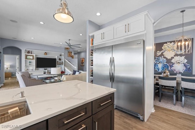 kitchen featuring arched walkways, light wood-style flooring, dark brown cabinetry, white cabinets, and stainless steel built in fridge